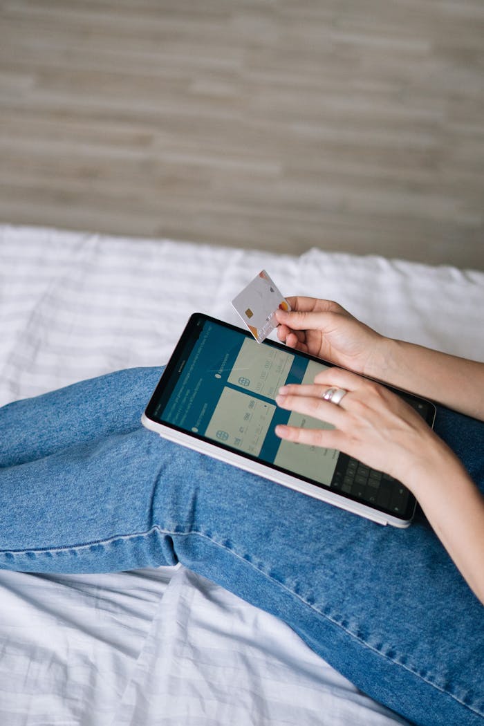 Person using a tablet and credit card for online shopping in a cozy home setting.